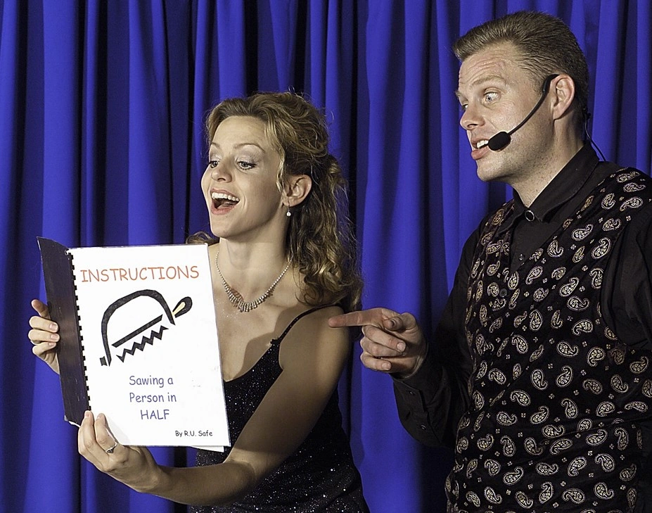 Comedy magician Brock Edwards and his dancer reading sawing-in-half instructions on stage