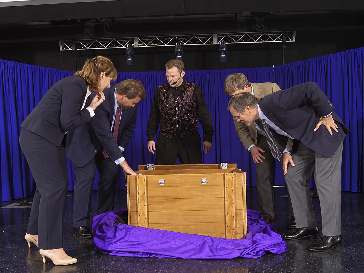 Corporate comedy magician Brock Edwards on stage with four business-suited volunteers inspecting a crate